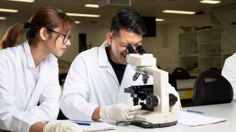 Students in Science Lab with white coat, goggles and  microscopes